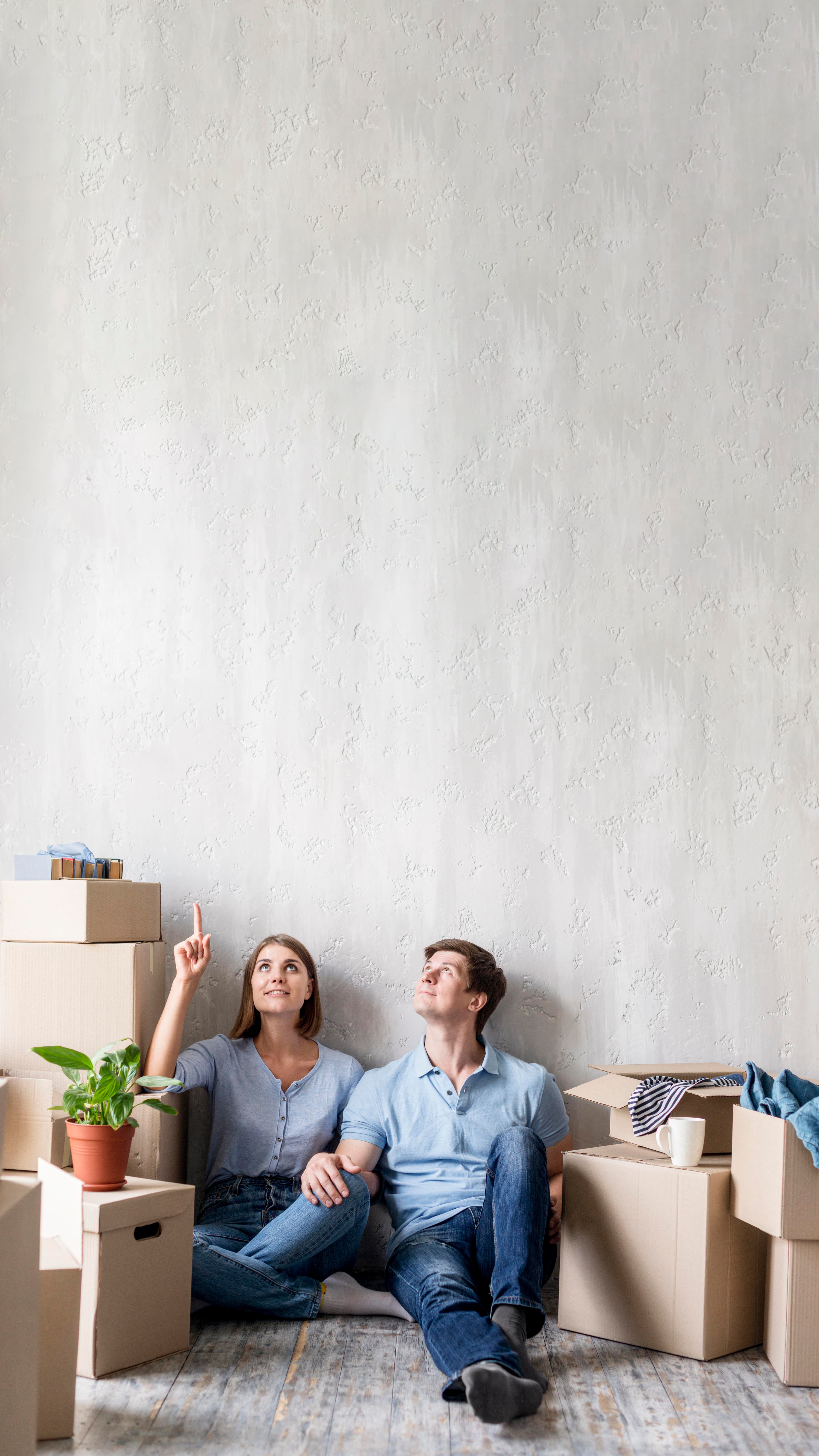 Una pareja sentada en el piso entre cajas de mudanza, mirando su nuevo hogar